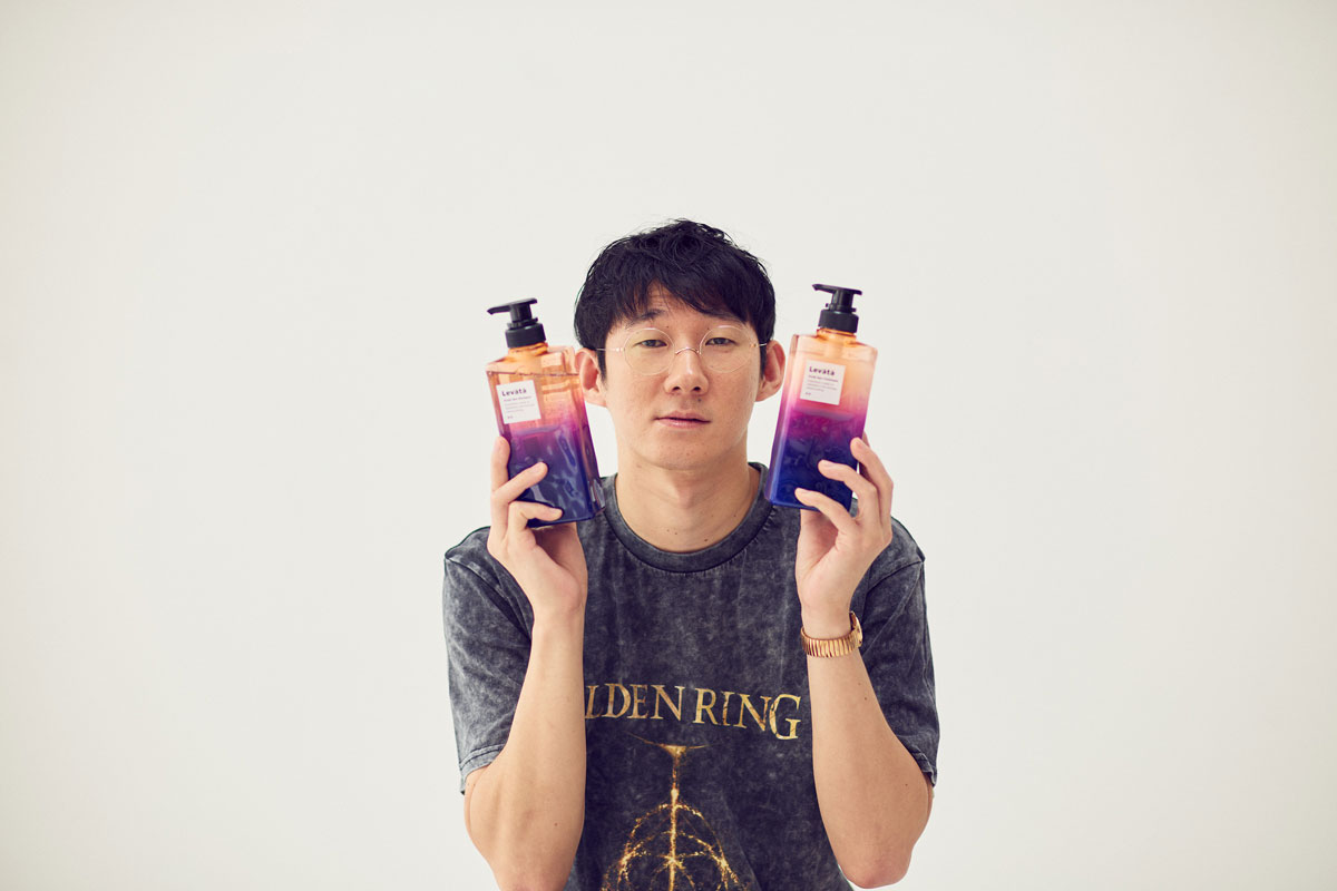 スカルプスパシャンプー〈レバタ〉を手に持つロングコートダディ堂前透