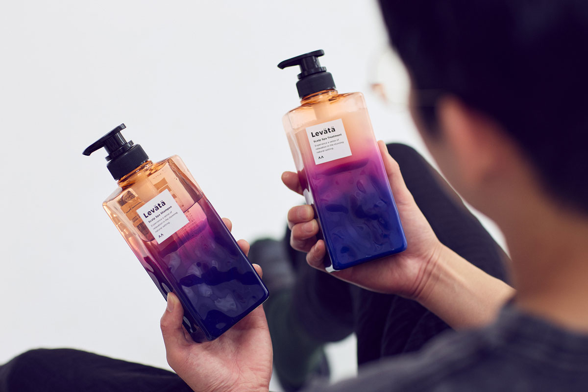 スカルプスパシャンプー〈レバタ〉を手に持つロングコートダディ堂前透