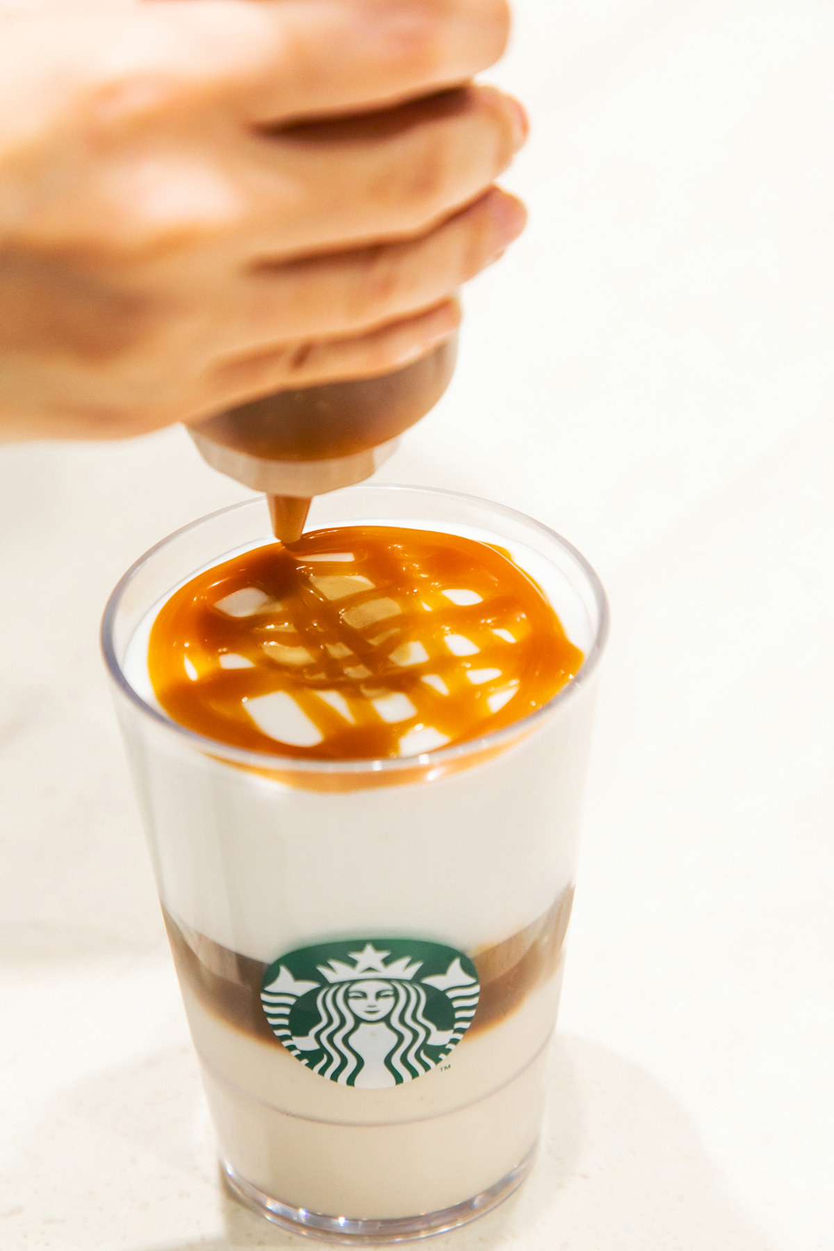 キャラメル・マキアートの仕上げにソースをかける様子